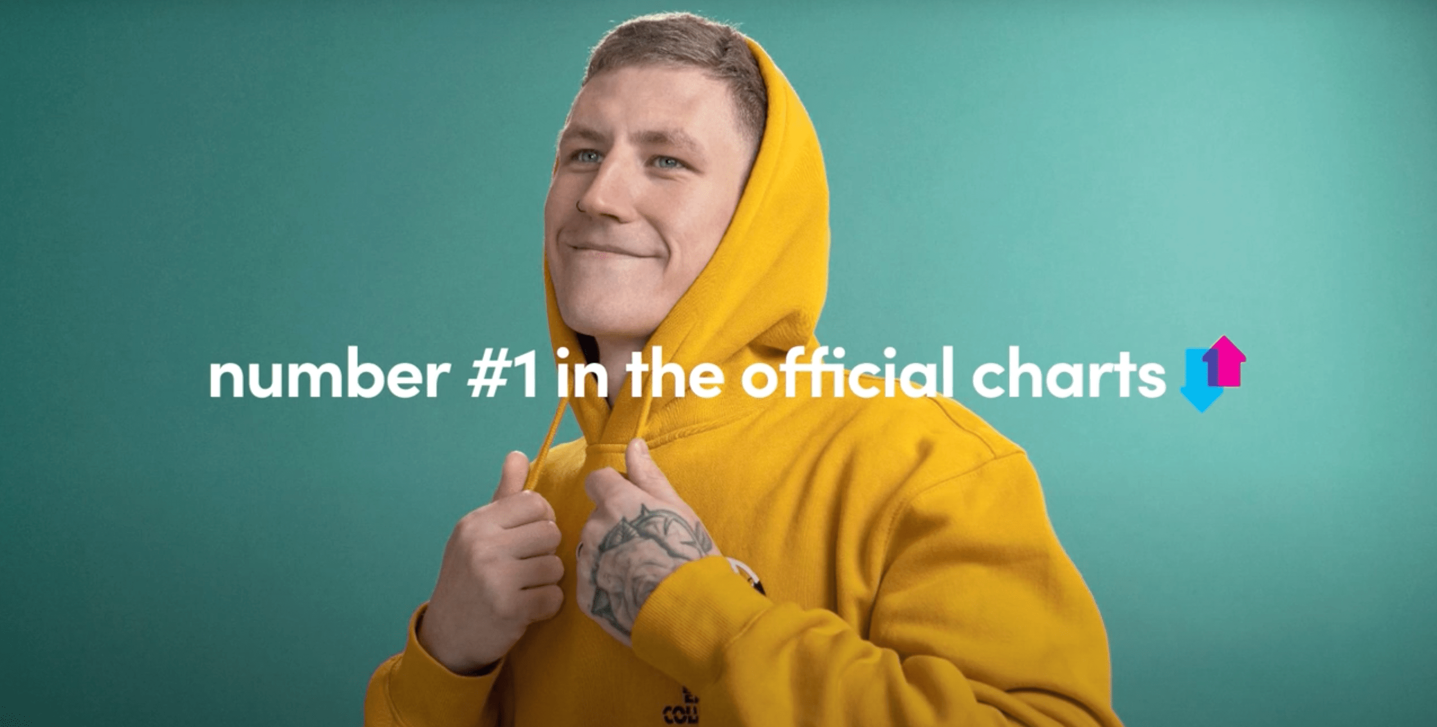 Nathan Evans in a yellow hoodie with the words number 1 in the official charts.